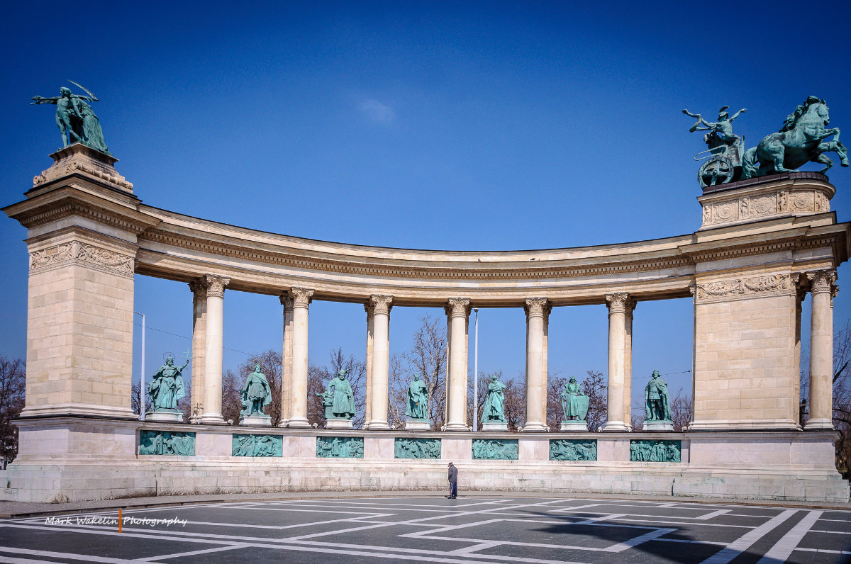 Millennium Monument in Budapest with classical statues and colonnade under a clear blue sky.
