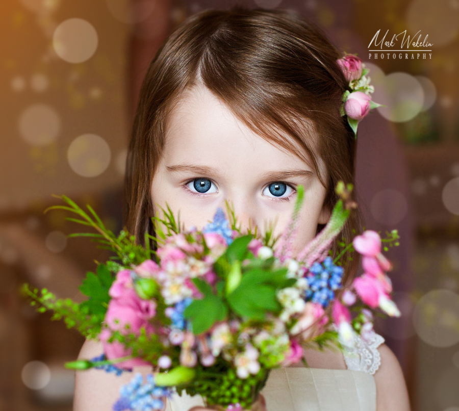 Young girl with blue eyes holding a colorful bouquet of flowers close to her face.