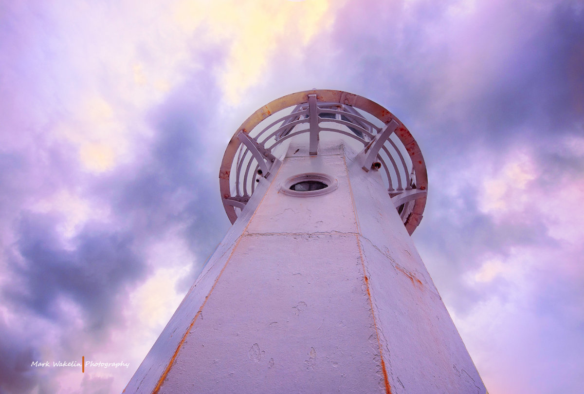 Low-angle view of a white lighthouse tower against a dramatic purple and yellow cloudy sky.