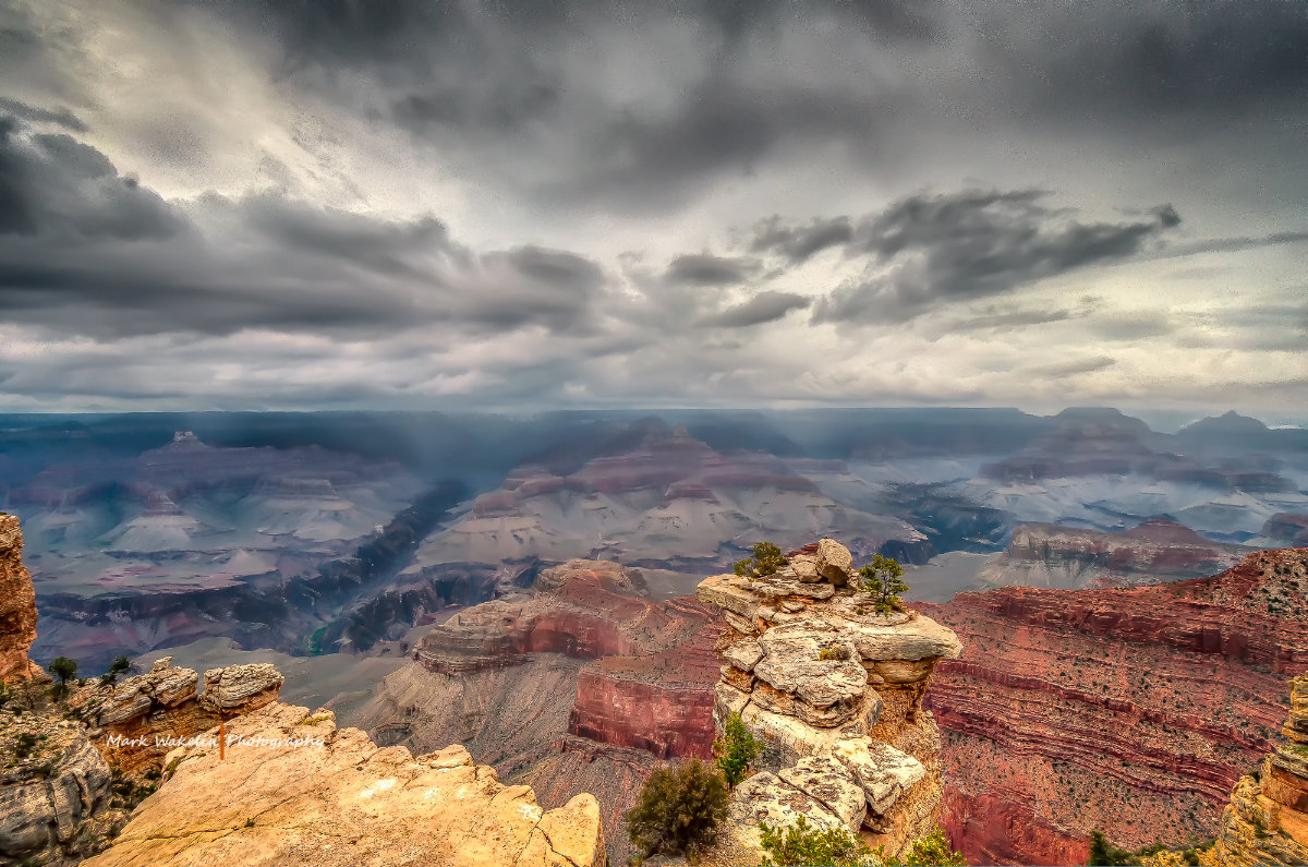 View of the Grand Canyon with layered rock formations under a cloudy sky with beams of light breaking through.