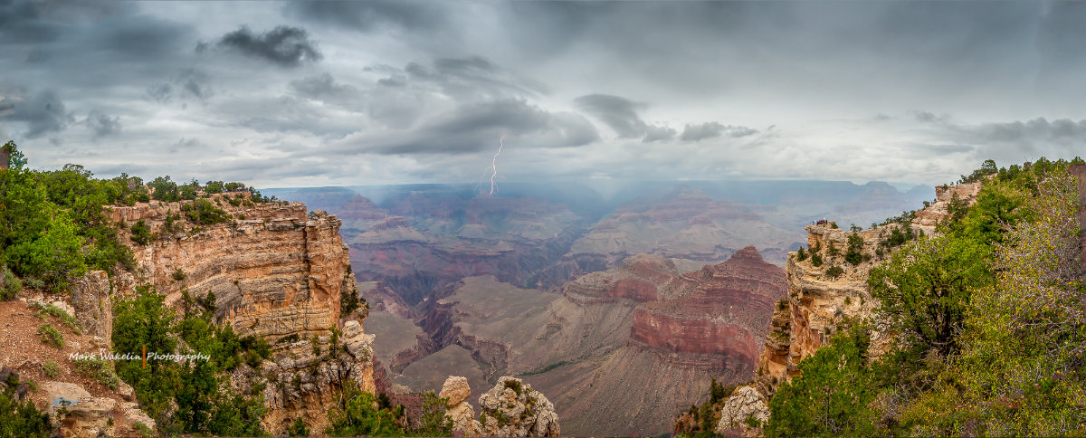 Panoramic view of the Grand Canyon with stormy skies and a lightning strike in the distance.