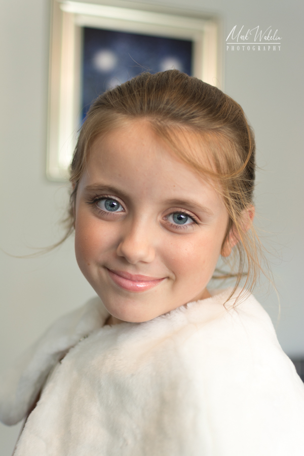 Portrait of a young girl with blue eyes and light brown hair, smiling and wearing a white fur coat.
