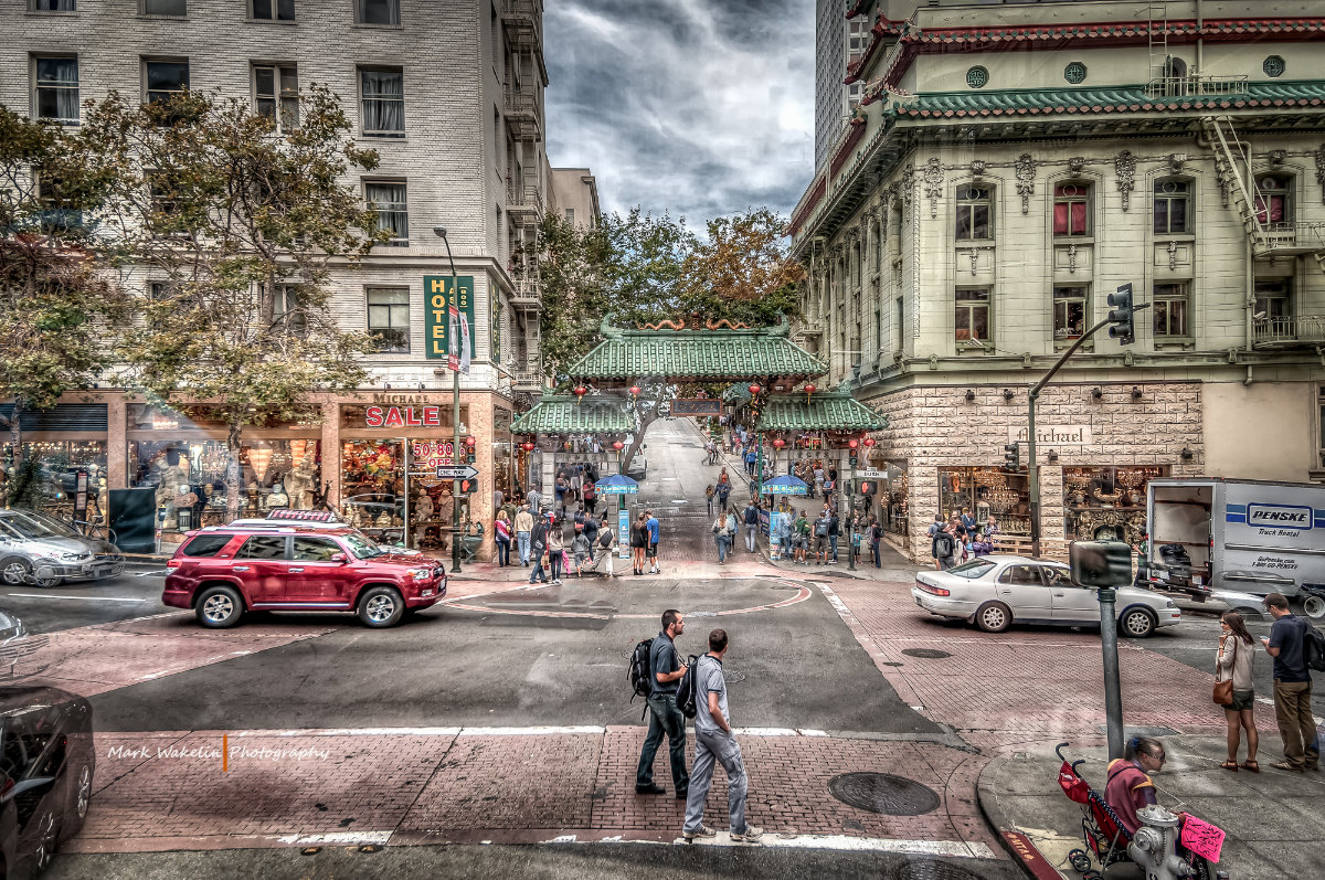Busy street scene in Chinatown with pedestrians, cars, and a traditional Chinese gate with green tiled roof in the centre.